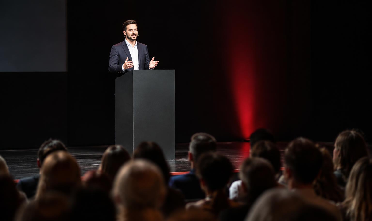 Speaker presenting on a dark stage with red accent lighting